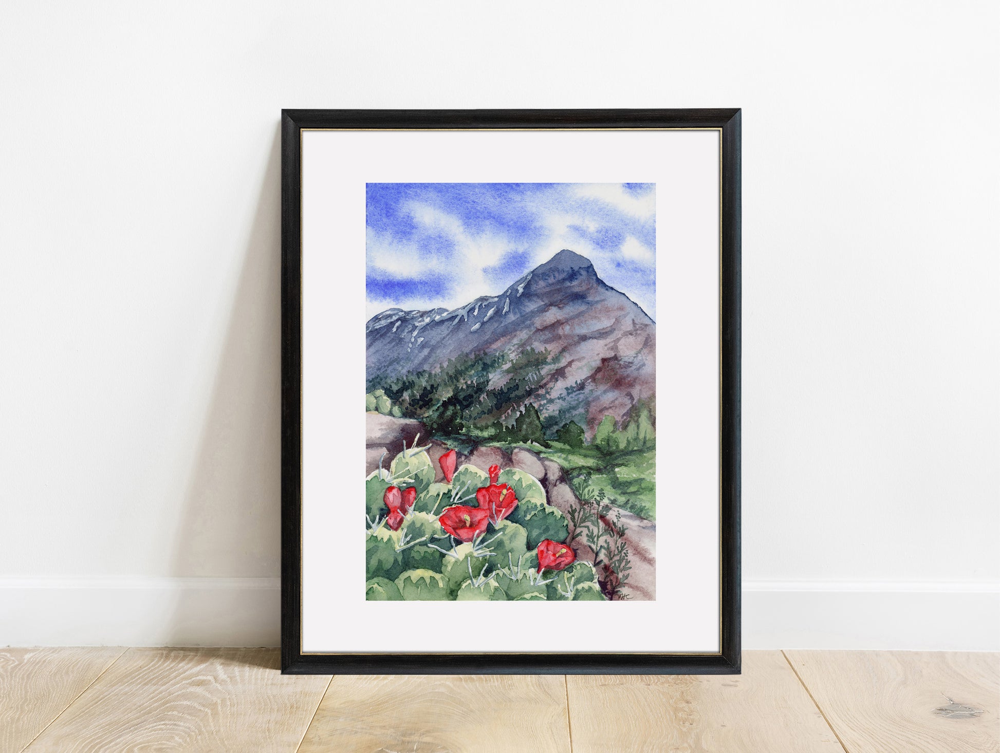 Framed watercolor painting of a mountain landscape with red claret cup cactus flowers on a white wall.