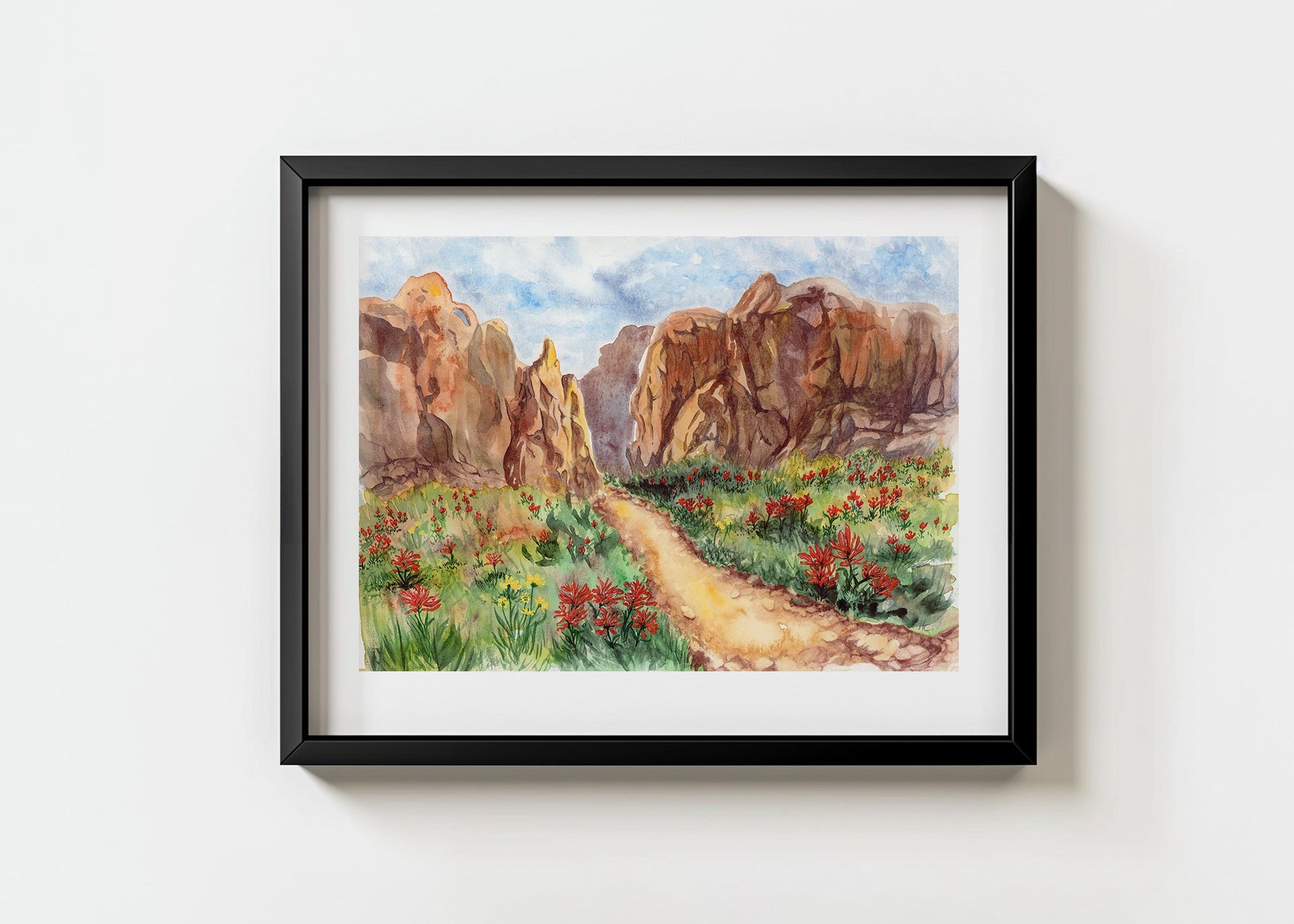 Framed artwork of a desert landscape with rocky canyon formations and a path through red and yellow wildflowers